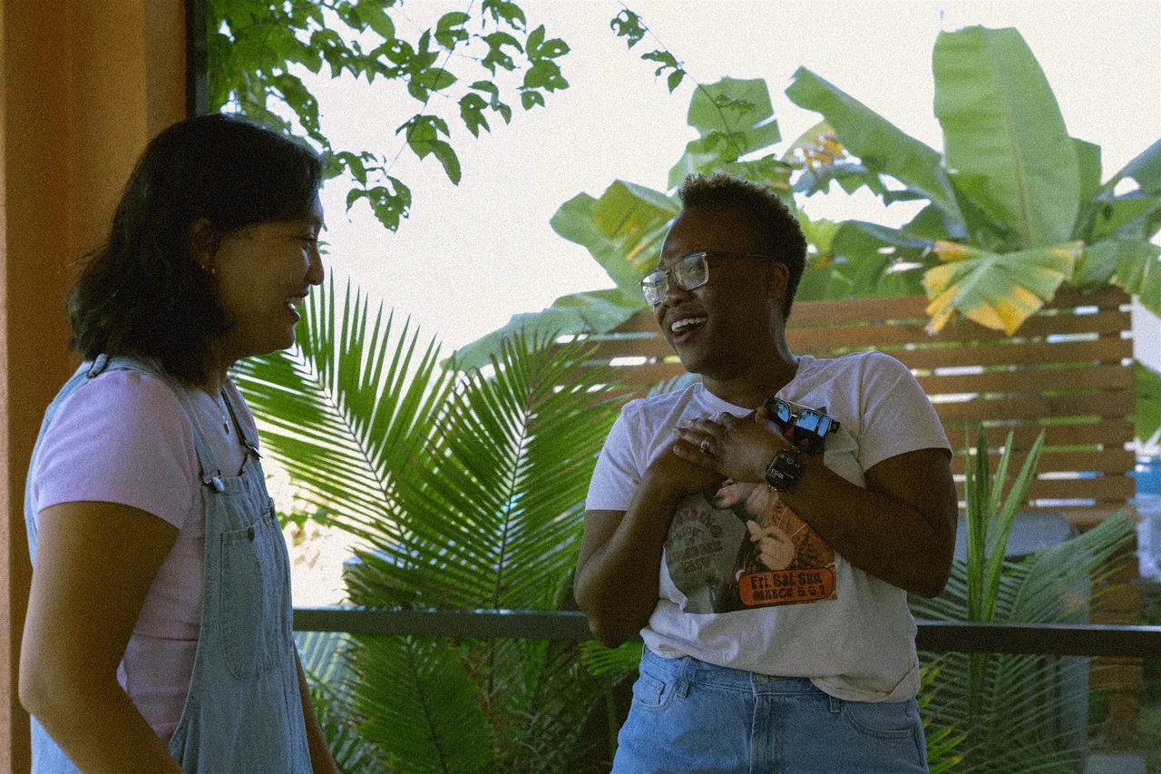Two friends laughing together on a plant-filled porch